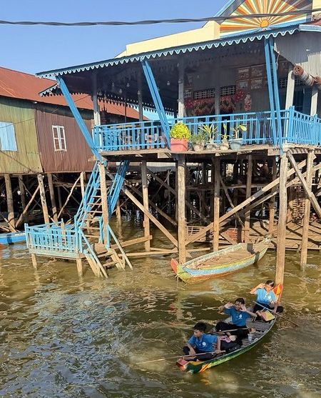 Three school children in a small canoe leaving a school on stilts surrounded by water