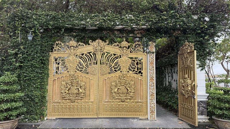 Very ornate double golden gate surrounded by greenery