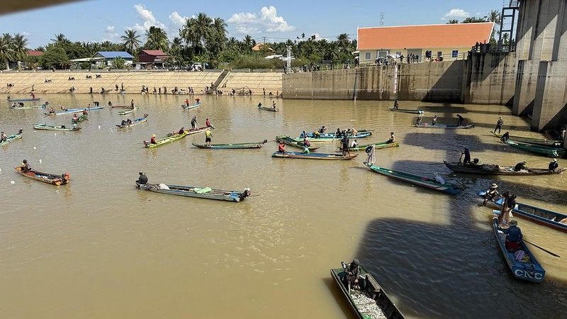 About 20 to 30 small colourful boats in the stream and on the banks of the stream loads more fishermen
