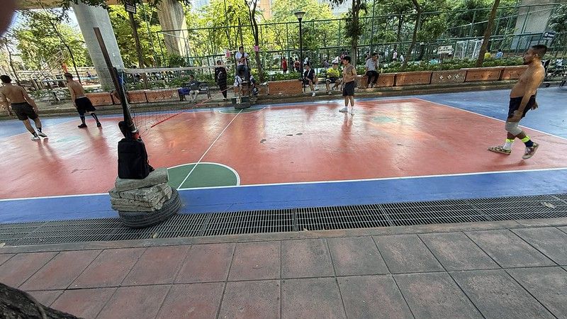 Some people playing sepak takraw in a park under a flyover