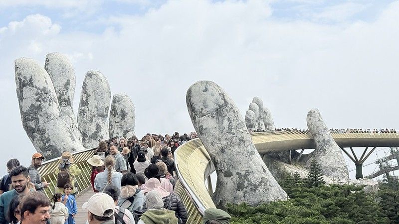 The Golden hand bridge now visible two stone hands holding a godeln bridge in the air, the bridge is full with 100s of people